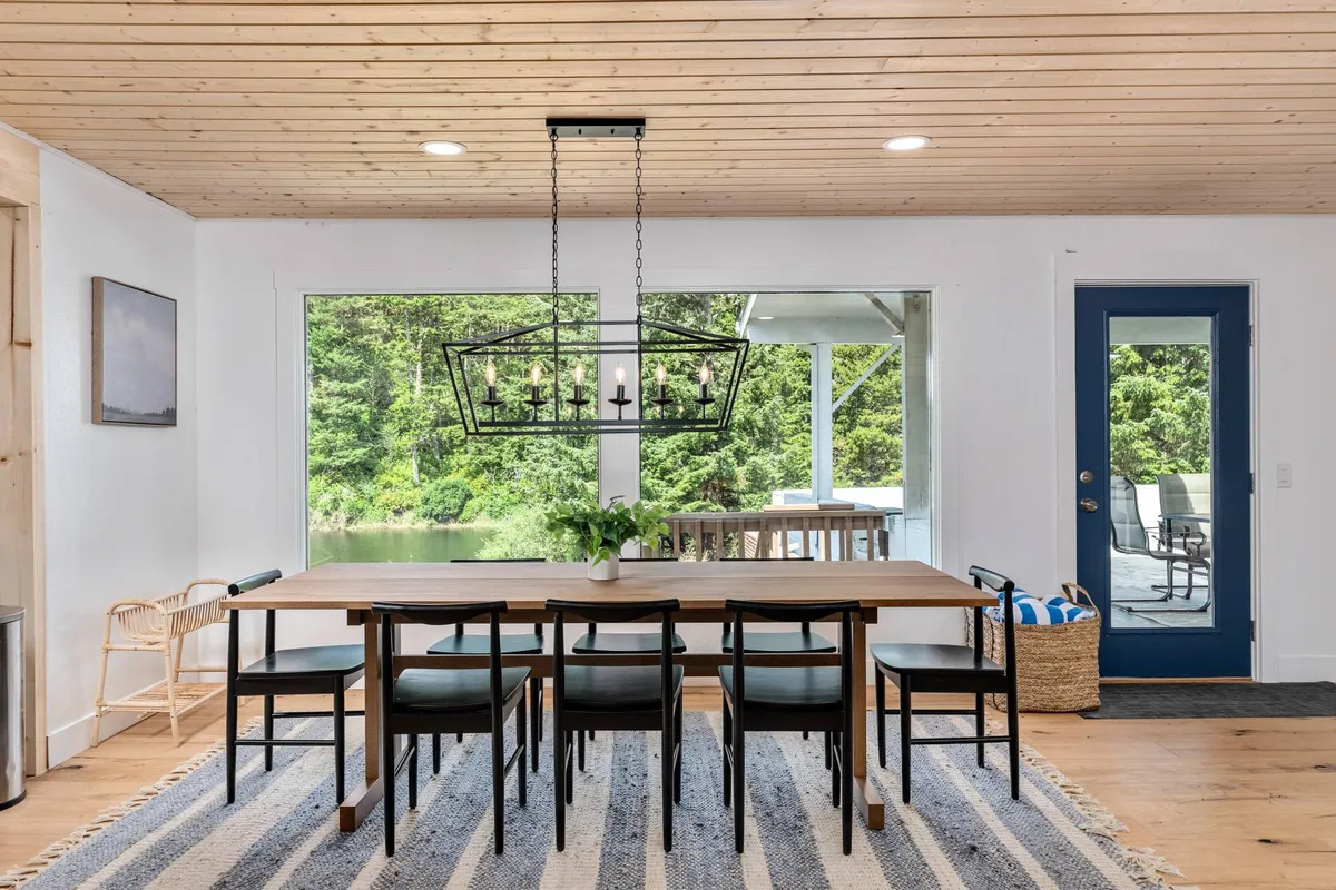 This image shows an elegant dining table beneath a stylish chandelier, framed by large windows that flood the space with natural light and offer a scenic outdoor view. The atmosphere is intimate and perfect for group meals or celebrations.