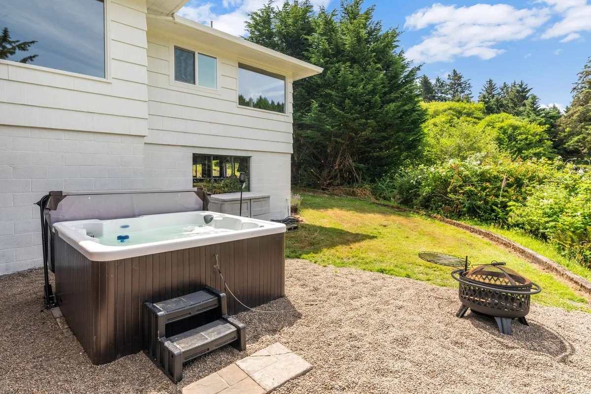 This image spotlights an outdoor hot tub and fire pit surrounded by lush greenery. The inviting atmosphere suggests sociable evenings and relaxing afternoons in the backyard oasis.