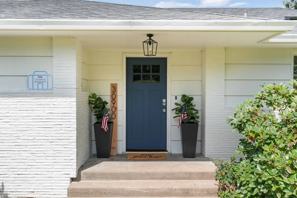 The front entrance of the property features a cheerful blue door, potted plants, a welcome mat, and a house number sign. The inviting outdoor space suggests a warm welcome and serves as the transition point between home and beach adventures.