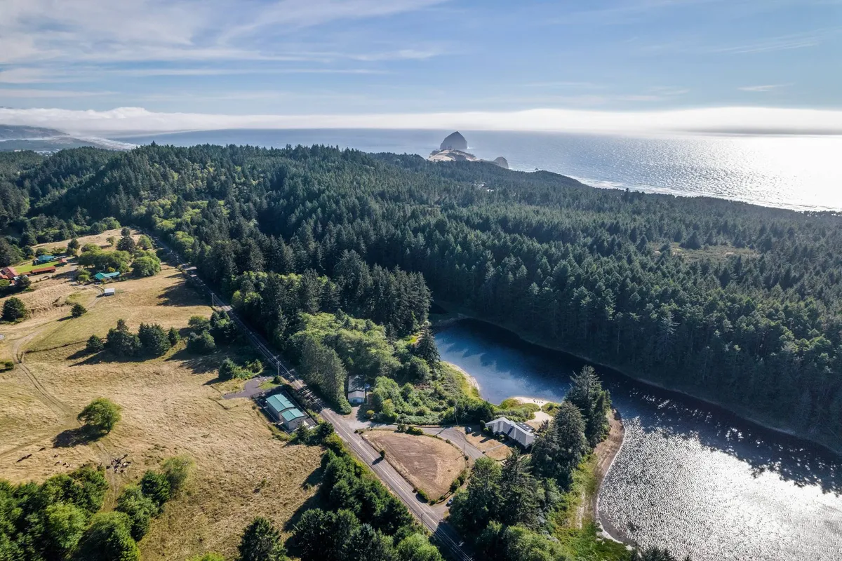 A sweeping view captures a serene body of water bordered by a forest canopy, rocky outcrop, and distant ocean horizon. The tranquil lake is the clear focal point, inviting visions of fishing, paddling, and quiet reflection amid nature. The peaceful water surface and surrounding greenery emphasize privacy and natural beauty.