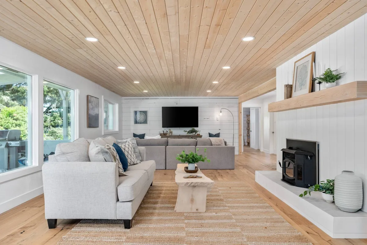 A bright, open living area with plush sofas centered around a coffee table and a cozy fireplace. Expansive windows allow natural light to flood in and offer clear views of the lake outside. The space exudes an inviting, comfortable atmosphere perfect for relaxation, socializing, or movie nights.
